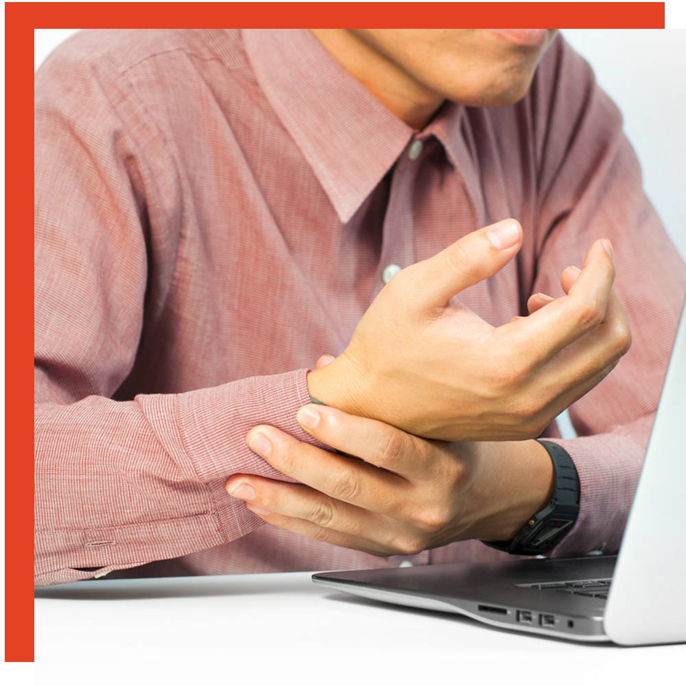 Man in a pink shirt gripping his sore wrist while working at a laptop