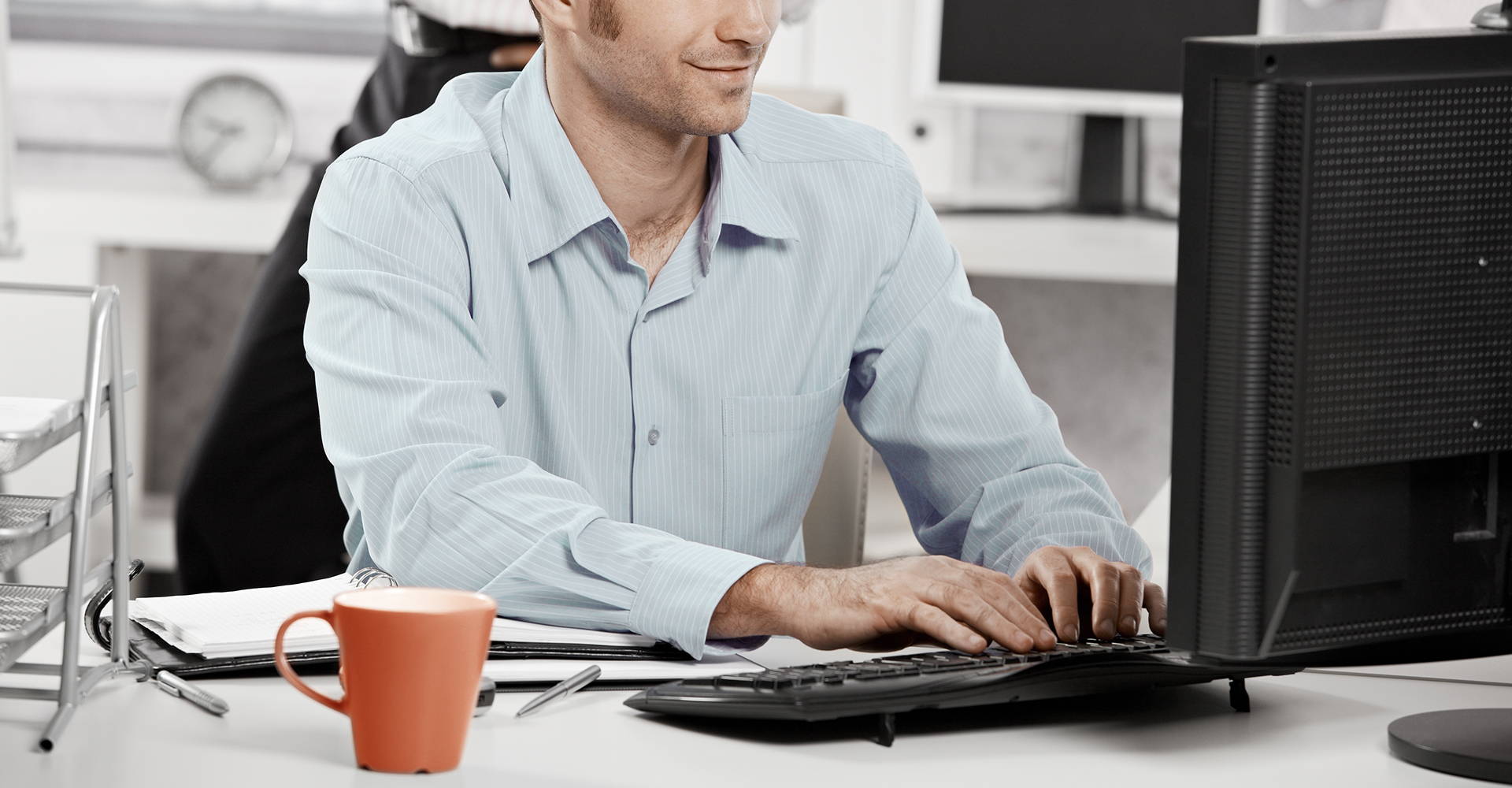 Smiling office worker typing at a desktop computer