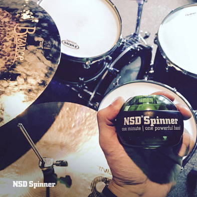 Hand holding an NSD Spinner over a drum kit