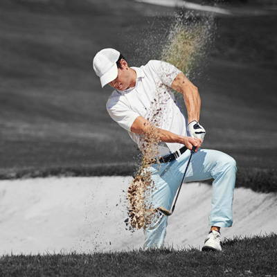 Golfer swinging out of a sand bunker in black and white
