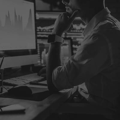 Man resting his head on his hand at a desk with several computer monitors