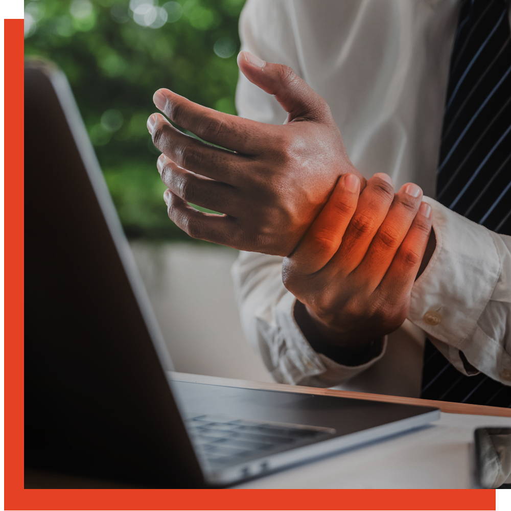 Office worker holding his sore wrist while working at a laptop